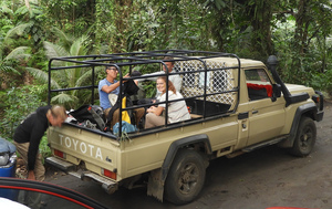 Toyota pickup truck equipped with a tubular cage over the back and three people seated in the cargo area